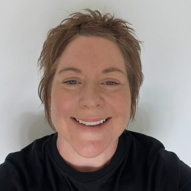 Smiling woman with short, light brown hair, wearing a black shirt, against a white background.